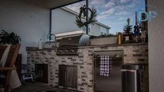 Outdoor kitchen with a built-in grill, tile backsplash, countertop, and a small refrigerator, under a clear sky.
