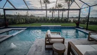Indoor swimming pool with a view of trees and water through large glass windows.