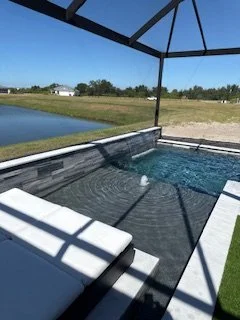 Screened pool enclosure with a view of a grassy field and pond, under a clear blue sky.
