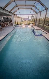 Indoor swimming pool enclosed with glass walls and ceiling, view of outdoor patio and landscape.