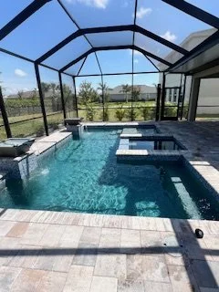Indoor screened pool area with a rectangular swimming pool, spa, and seating area, overlooking outdoor greenery.