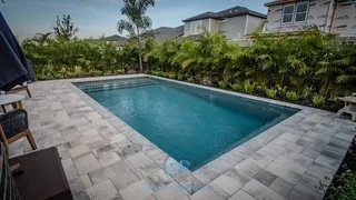 Swimming pool in a backyard with stone pavers and a green hedge