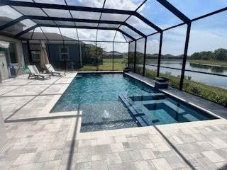 Enclosed backyard pool area with lounge chairs and a hot tub, overlooking a lake or pond.