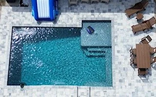 A swimming pool with a small step entry and lounge chairs on the surrounding deck.