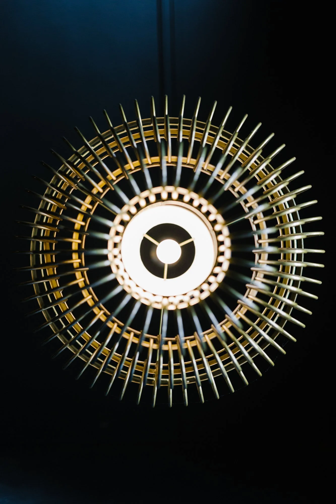 Close-up of a modern hanging pendant light fixture with circular metal design and a glowing light in the center, against a dark background.