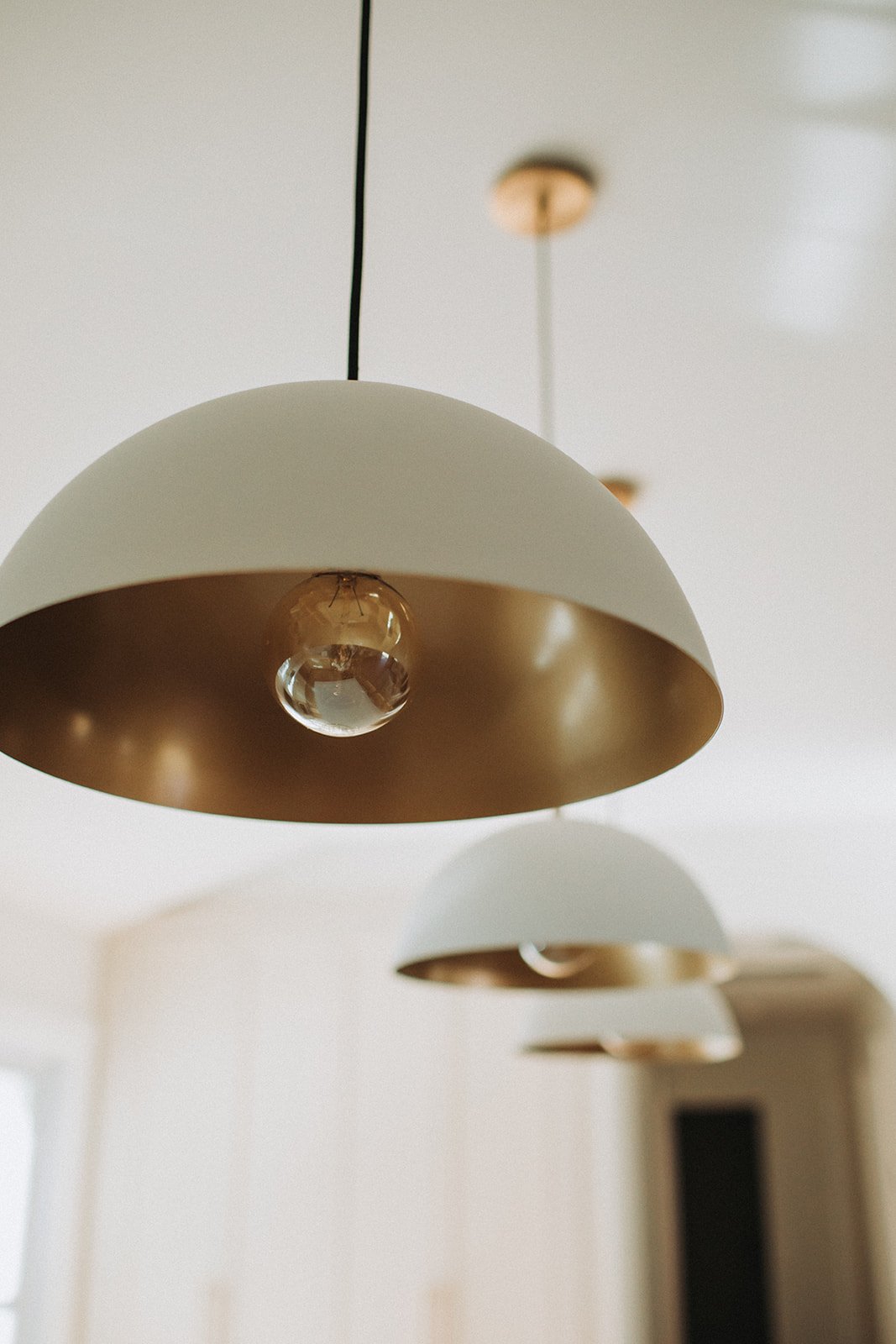 Close-up of modern pendant light with white and gold-colored shade and a small glass globe inside, hanging from a black cord.