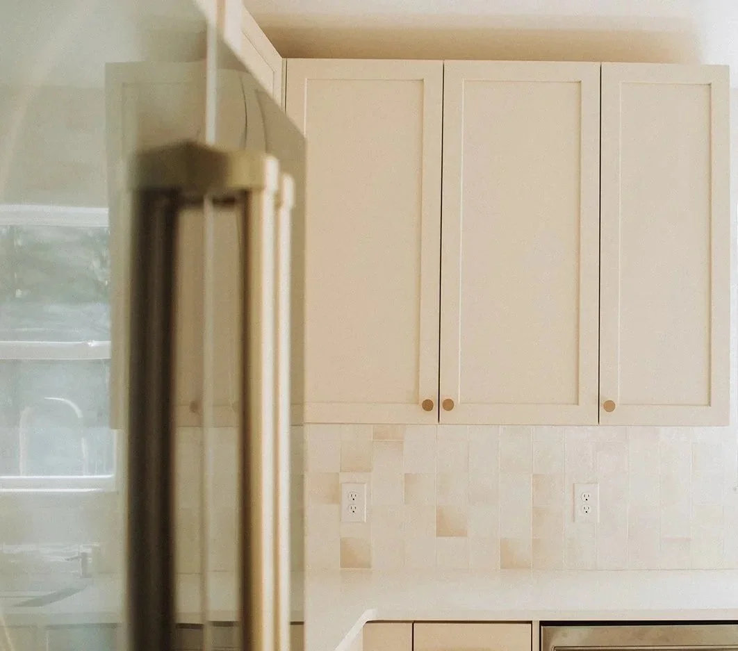Part of a kitchen with a beige refrigerator on the left, and beige cabinets with round knobs on the wall behind.