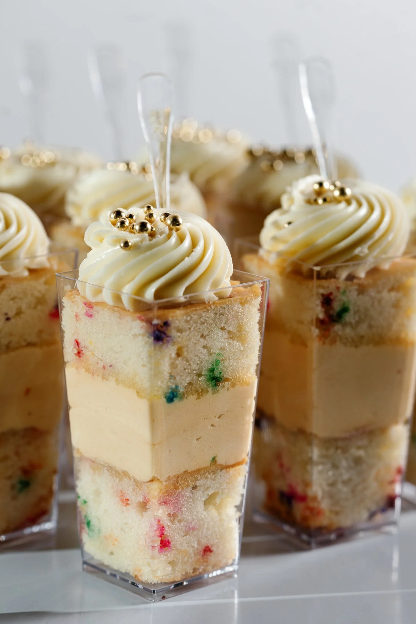Mini cake trifles in cups with buttercream swirl icing and gold ball sprinkles