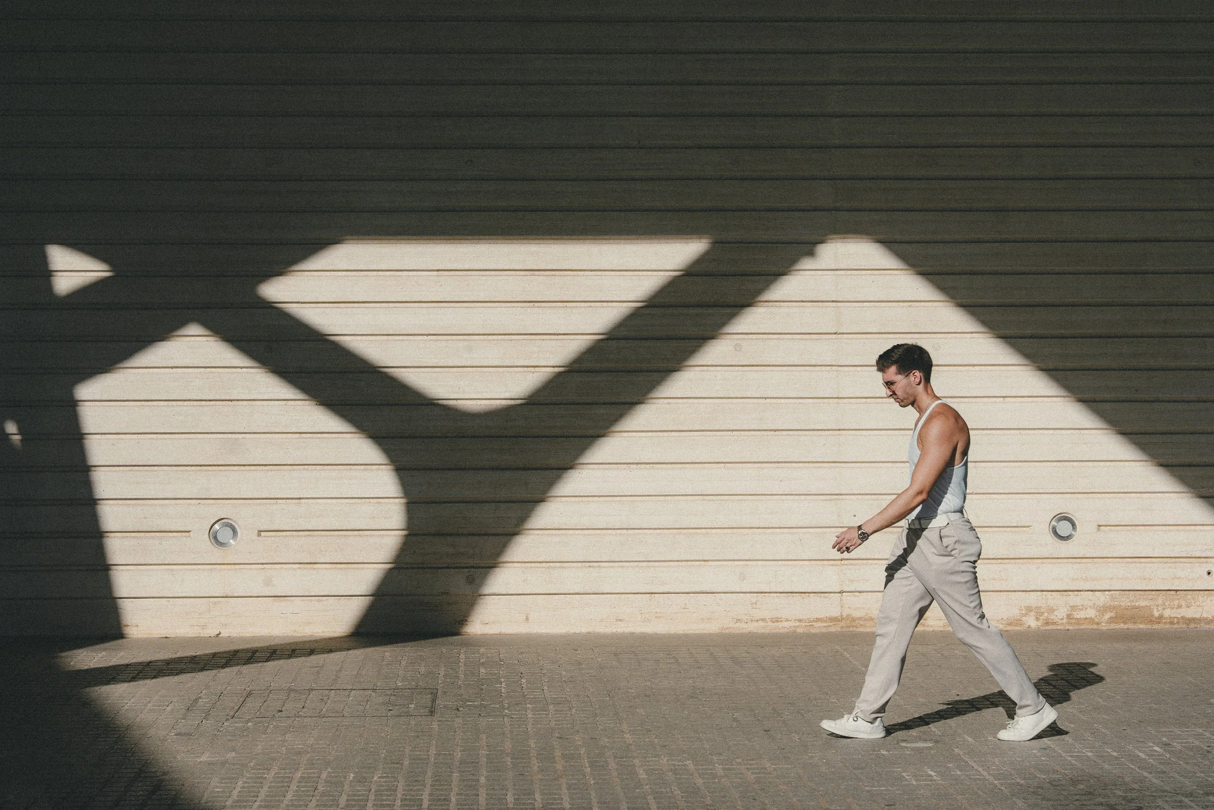 A man with glasses walking past a wall with his shadow cast on it, in the late afternoon sunlight.