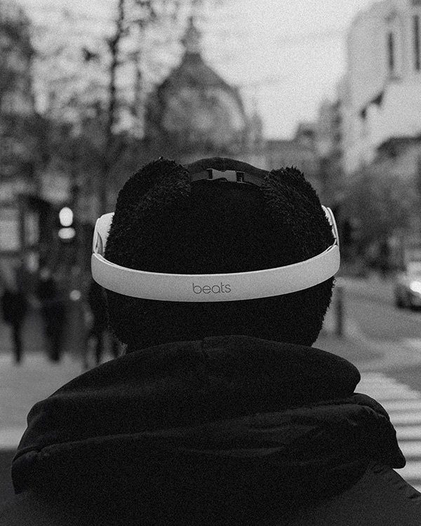 A person wearing Beats headphones with bear ears, standing on a city street during daytime, back view, black and white photo.