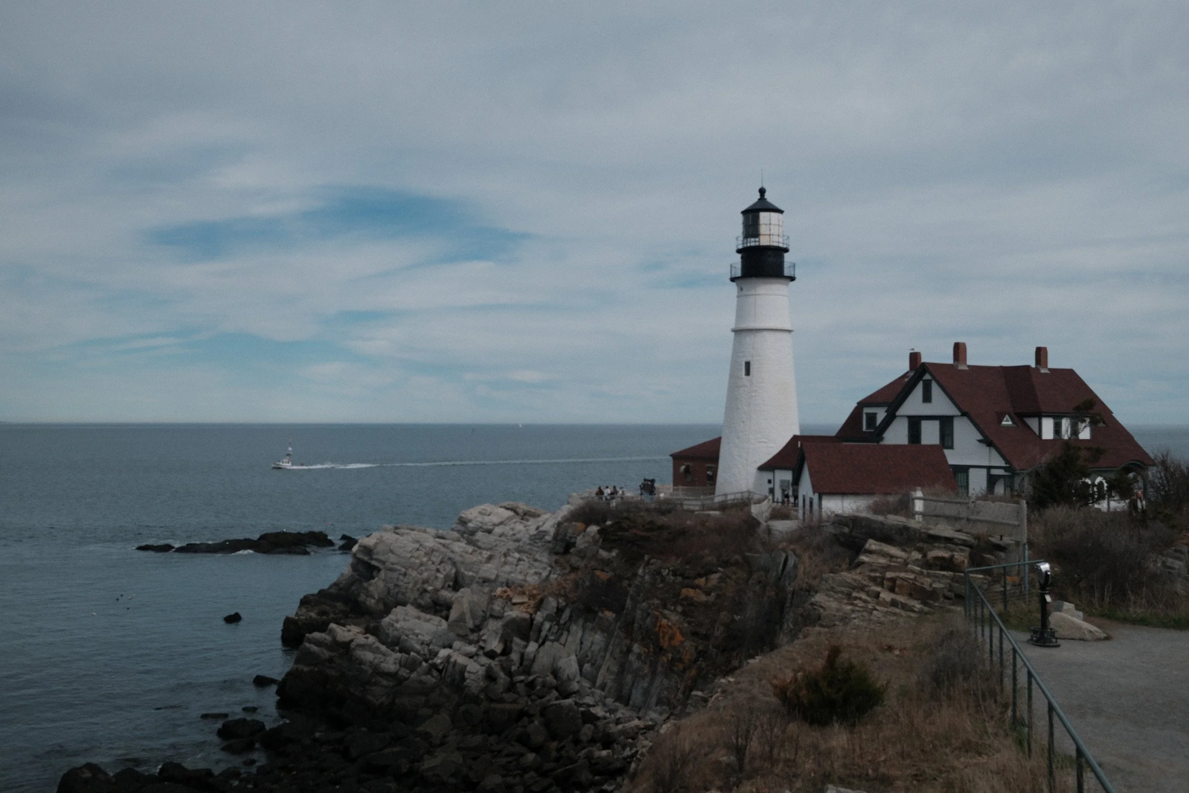 Coastal Beacon — A white lighthouse and red-roofed keeper buildings overlook a rocky coast and calm sea.