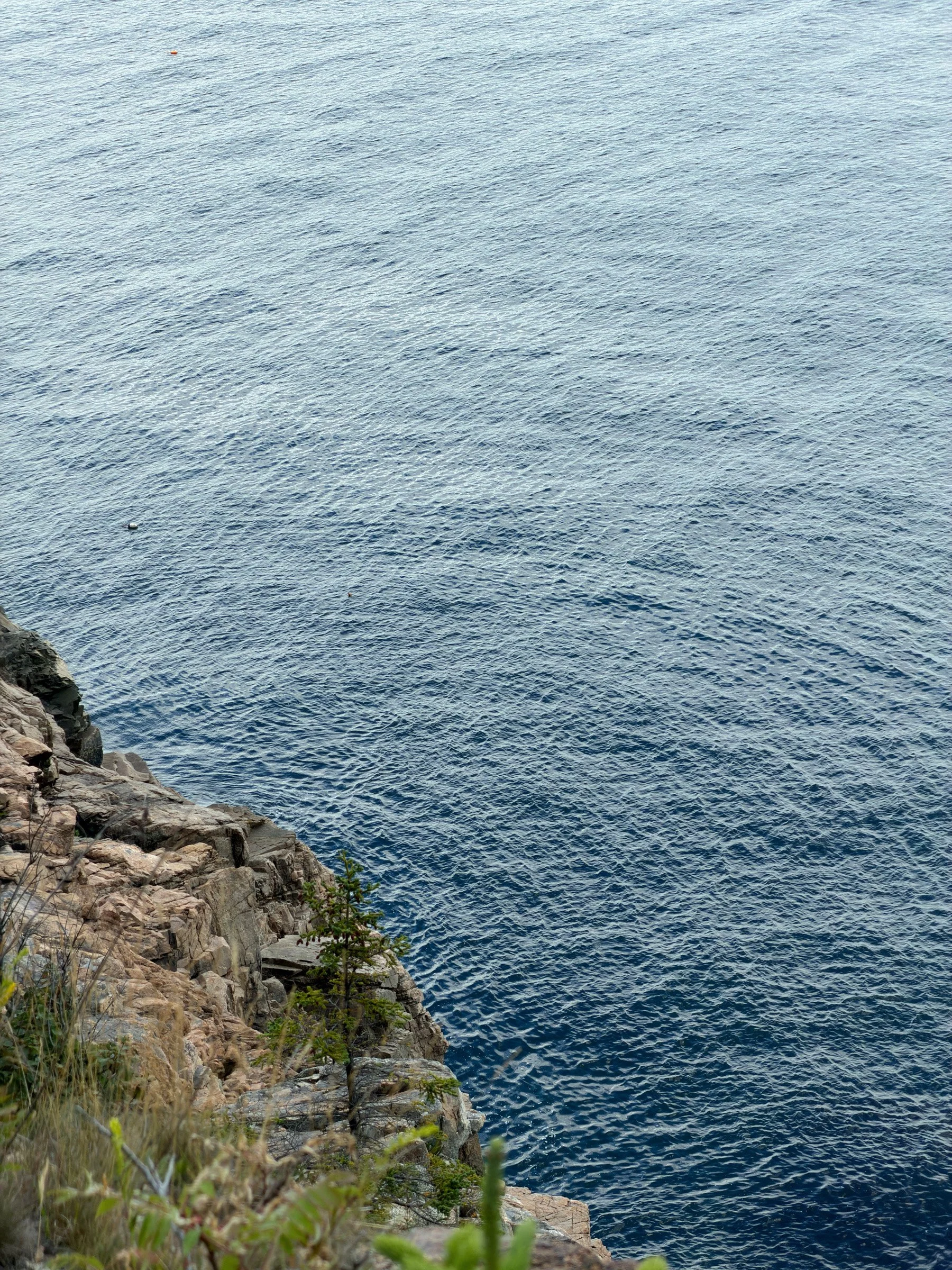 Stone and Water — A rugged rock ledge enters from the lower left beside a wide expanse of rippling blue water.