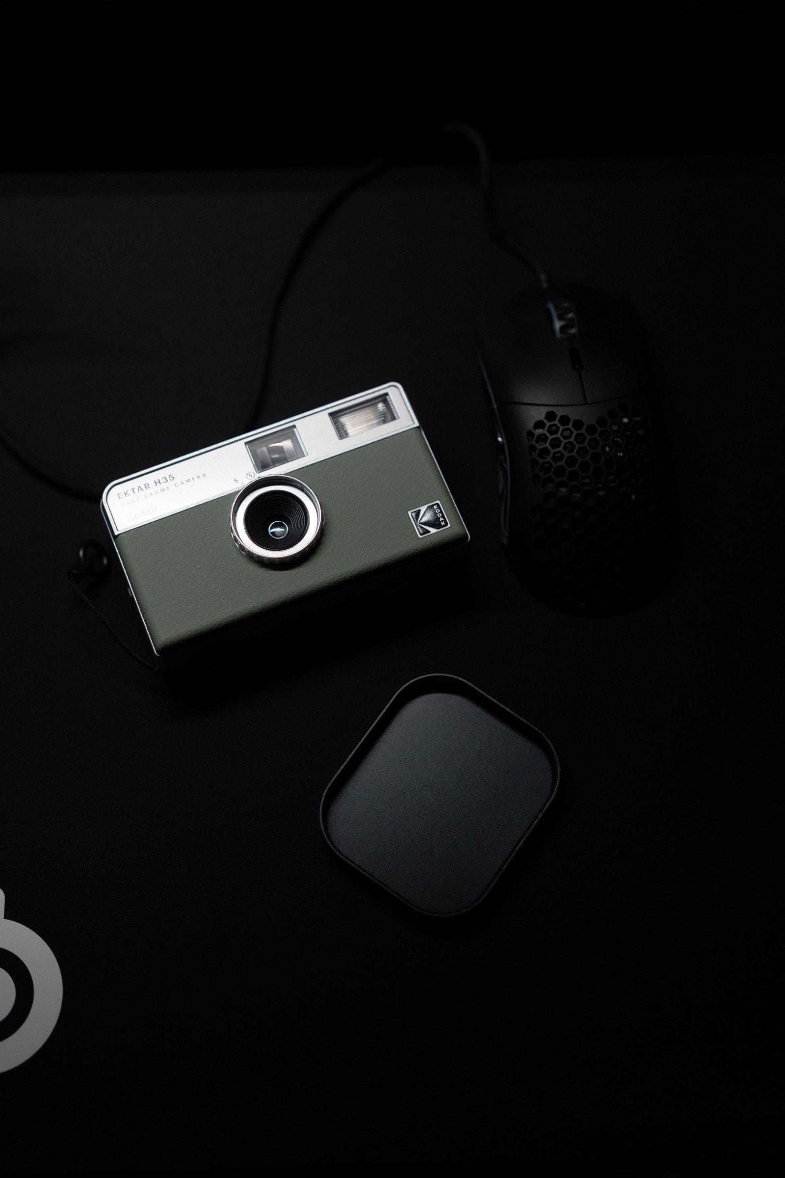 Quiet Frame — A compact film camera, mouse, and small case rest on a dark desktop.
