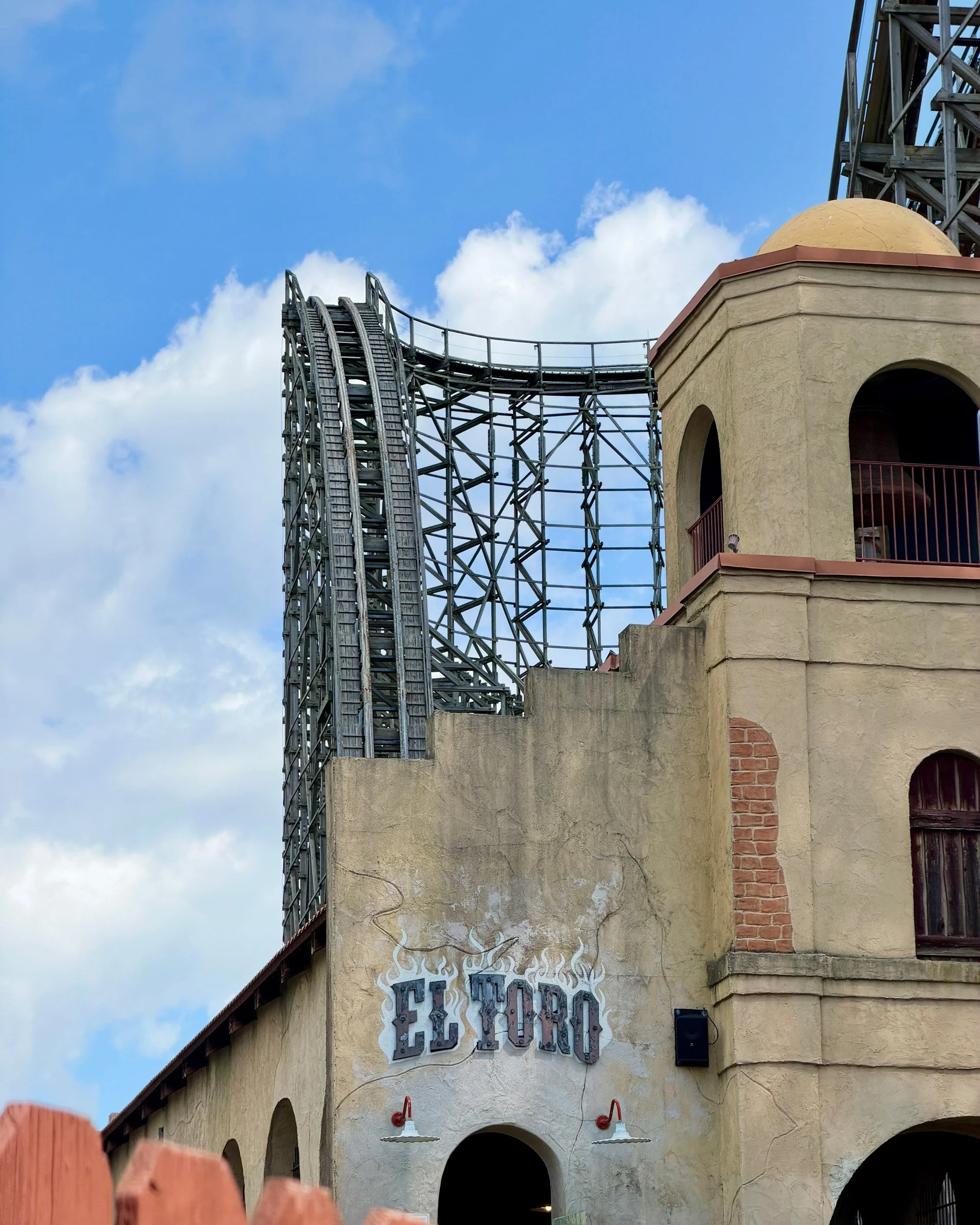 El Toro — A wooden roller coaster rises behind the weathered El Toro facade and a domed tower under a blue sky.
