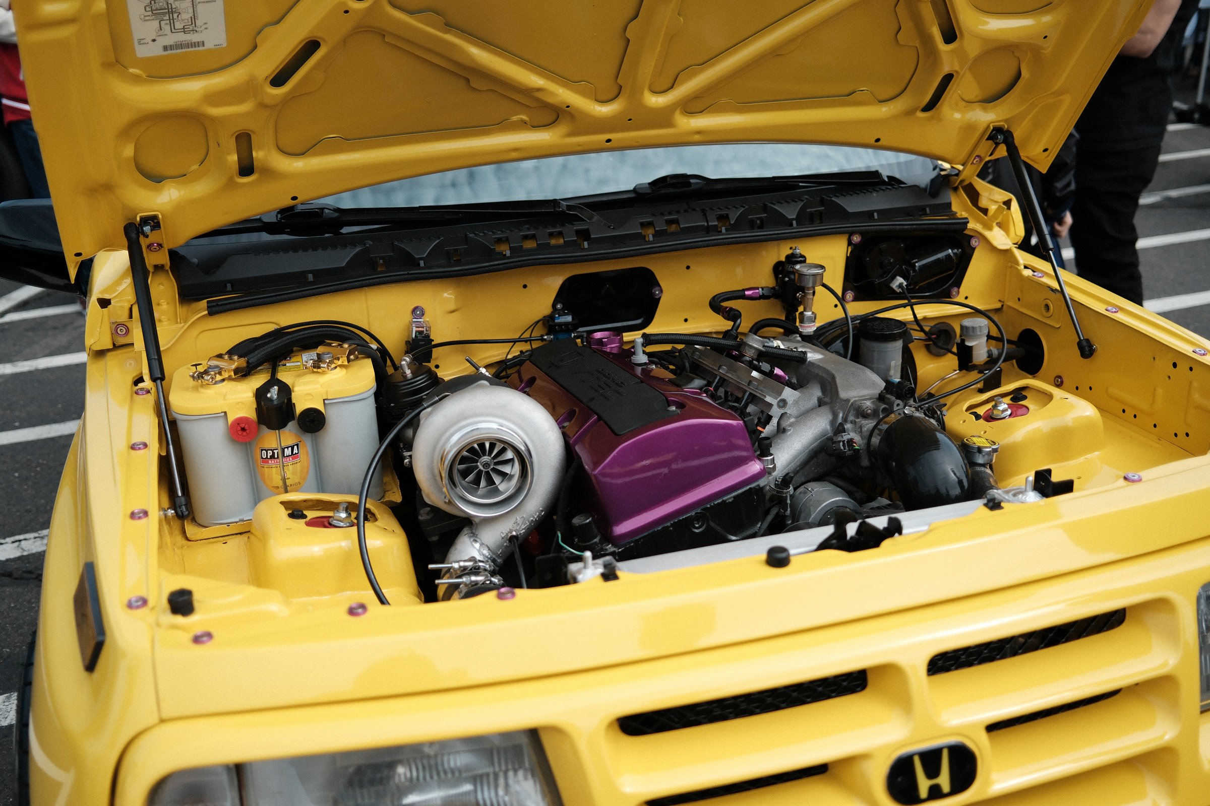 Under the Hood — A turbocharged engine with a purple valve cover sits inside a bright yellow Honda engine bay.