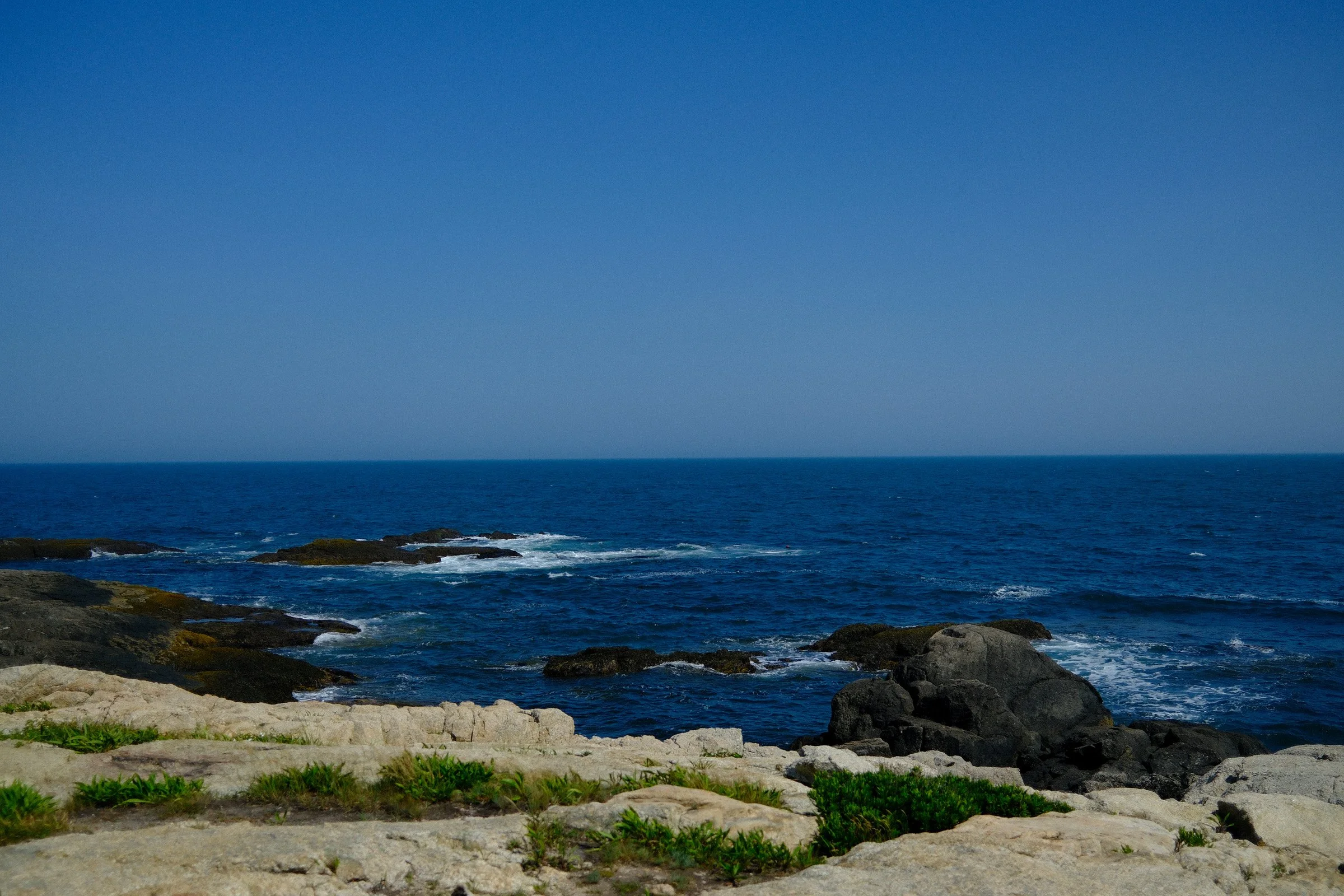 Atlantic Blue — Blue ocean waves break around coastal rocks beneath a clear sky.