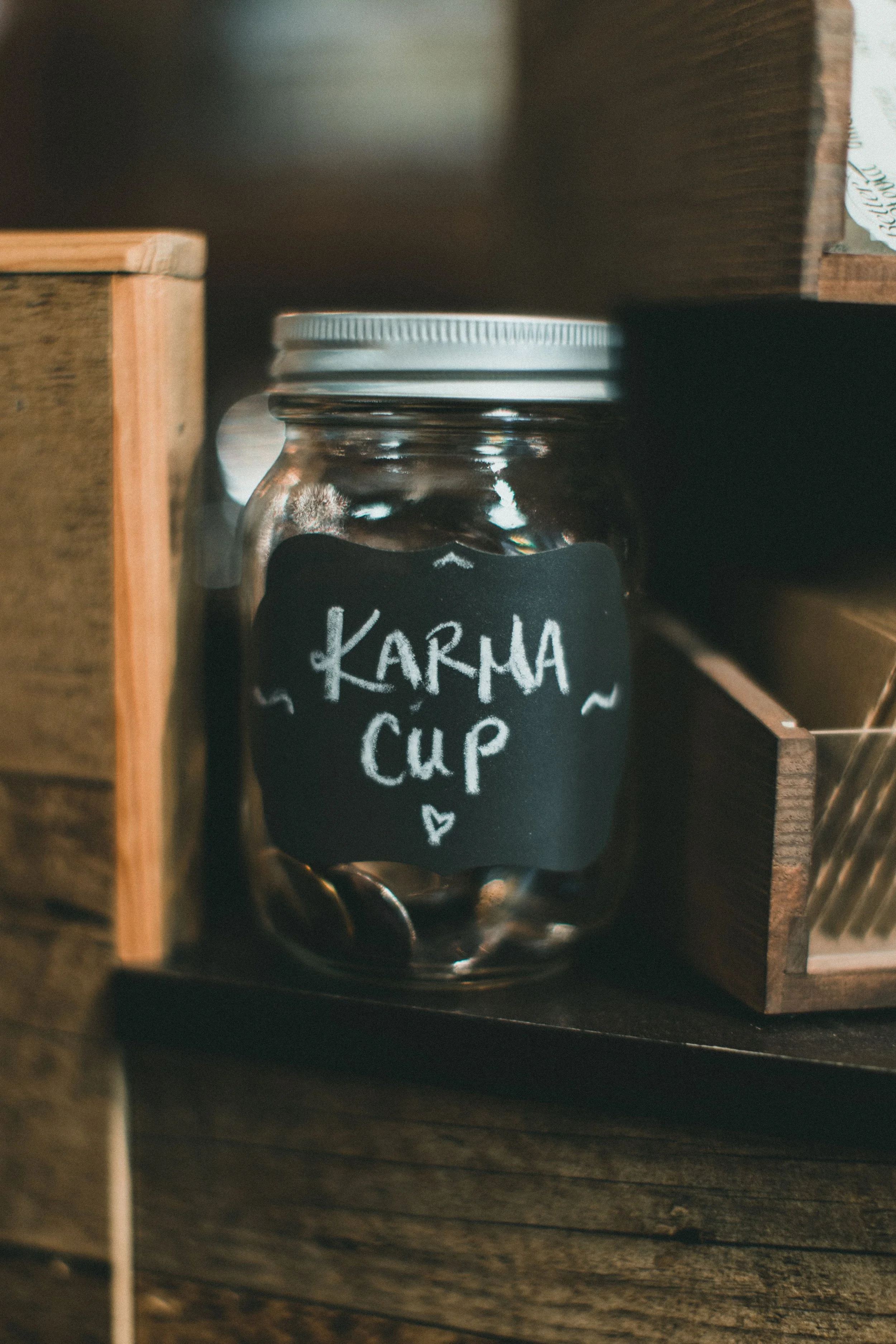 A glass jar with a white lid, labeled 'KARHA CUP' with a small heart, placed inside a wooden shelf with other shelves on either side.