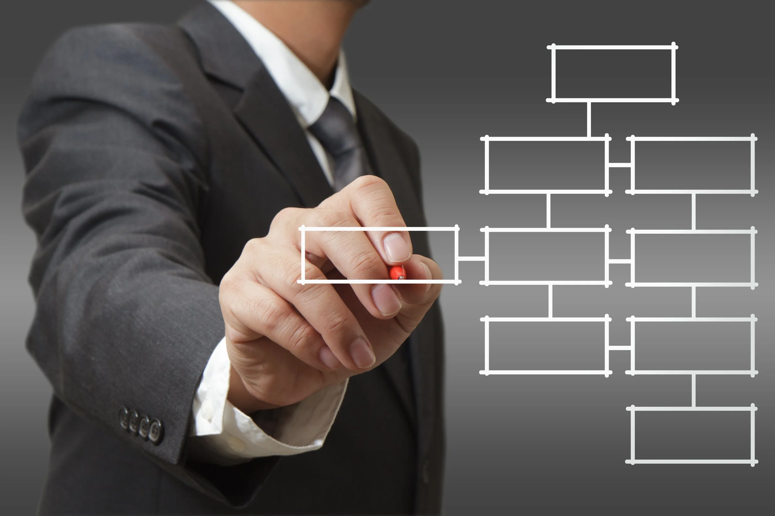A person in a business suit drawing an organizational chart or flowchart on a transparent surface with a red marker.