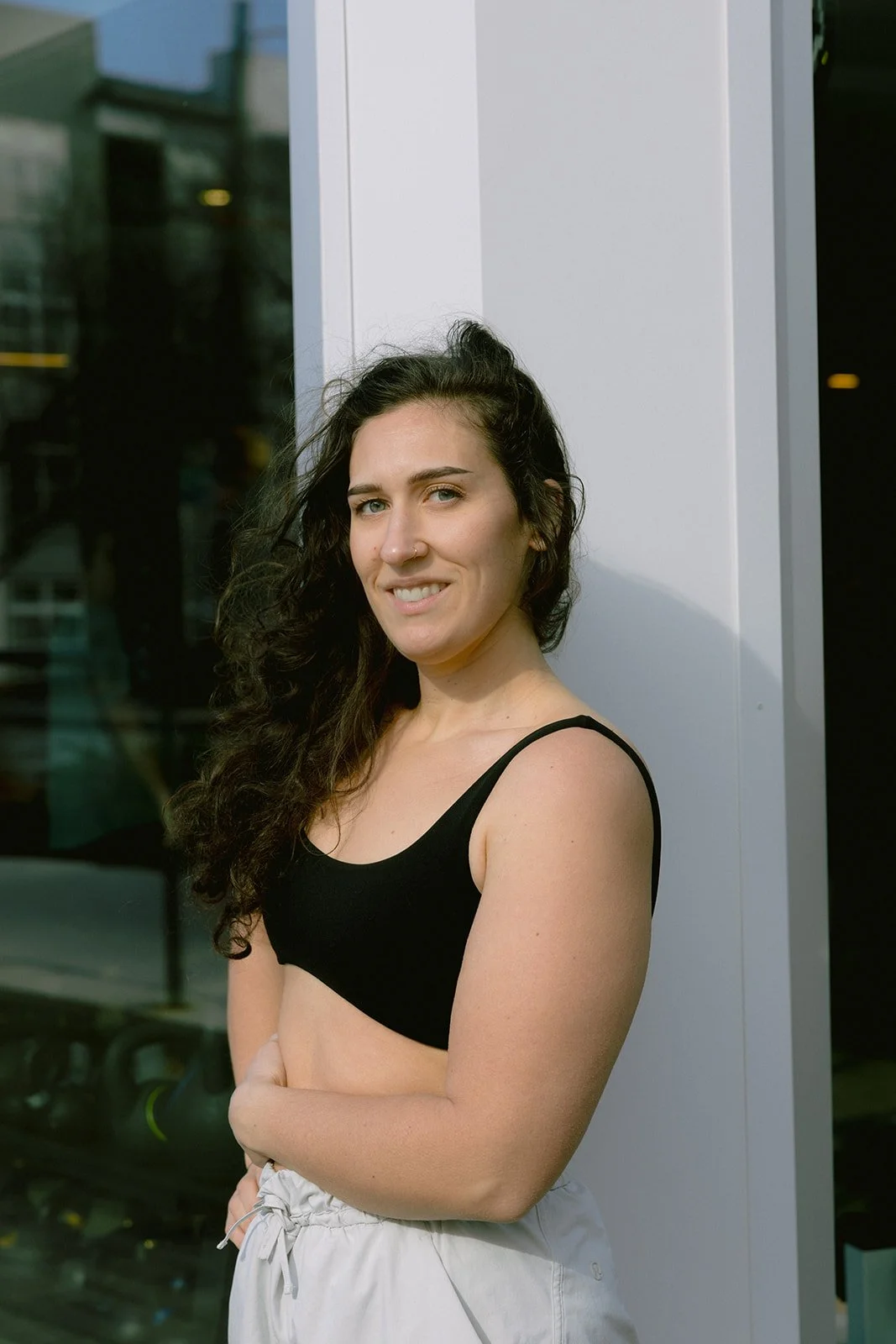 A woman with curly hair and light skin wearing a blue sports bra and black athletic leggings in a gym