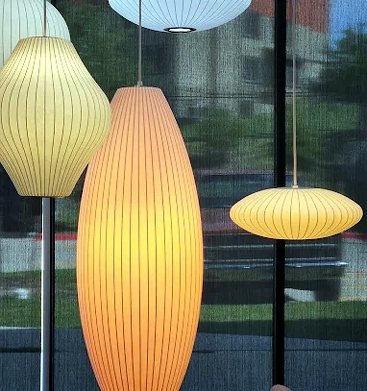 Three hanging paper lamps in different shapes and warm colors, with a dark background and a window showing a blurred outdoor scene.