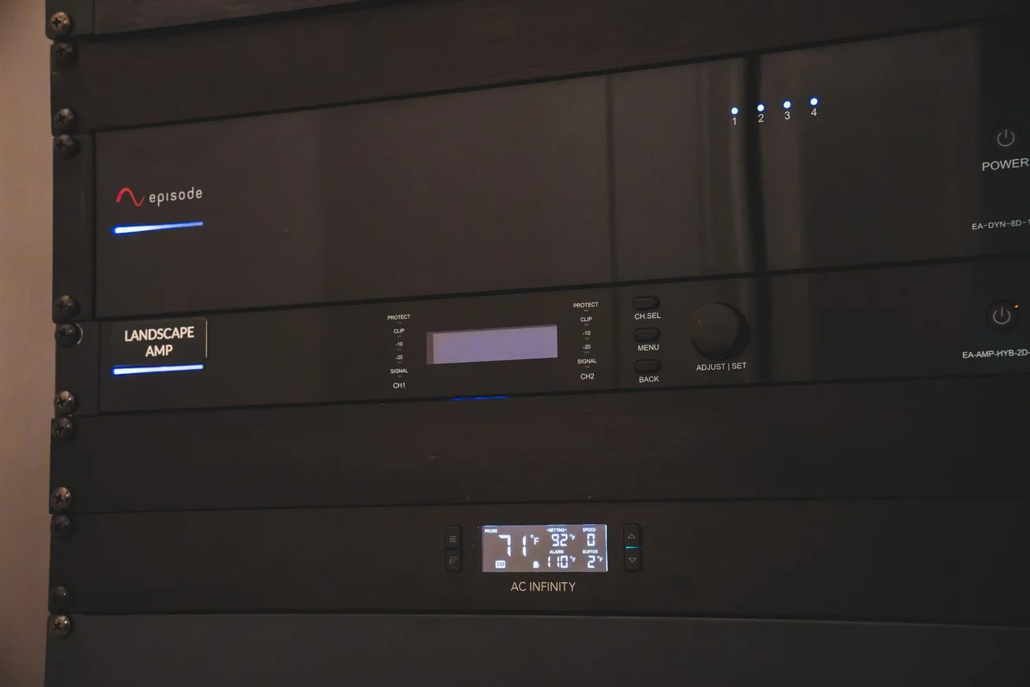 Equipment rack with a multi-channel amplifier and a thermostat-controlled fan controller below it