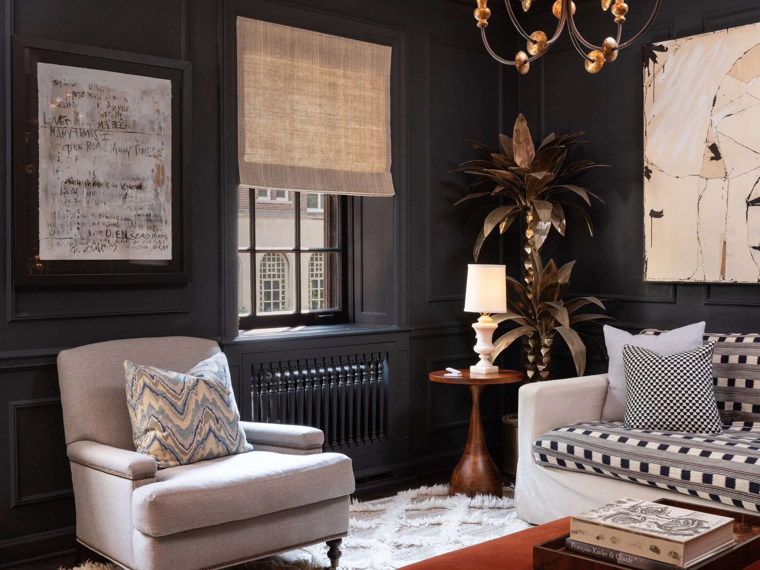 A sophisticated living room with Lutron lighting and shading control designed to balance comfort and style. The space features dark paneled walls contrasted by neutral furnishings, including a cozy armchair with patterned pillow and a sofa with bold