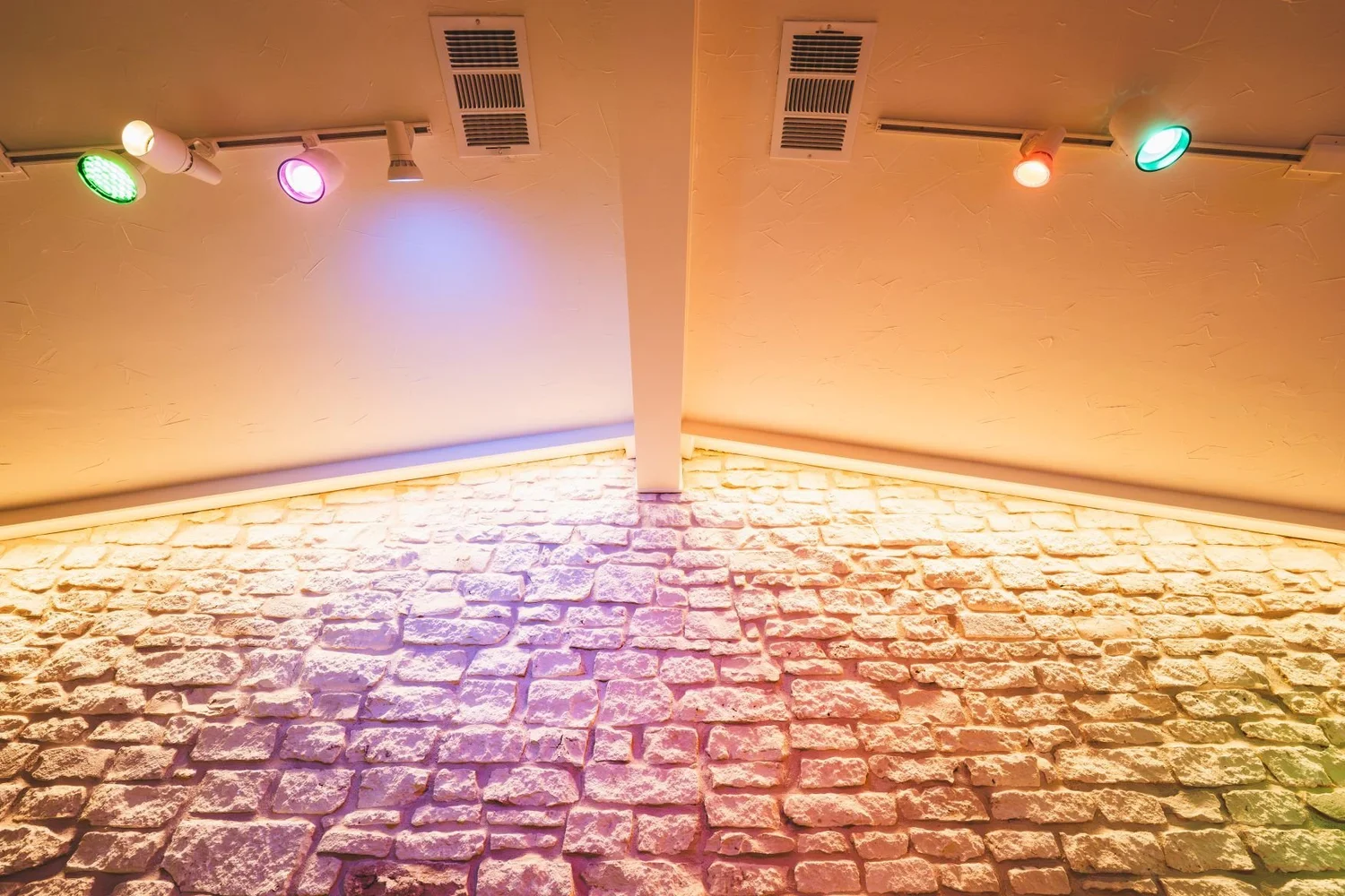 Stone wall washed with warm cove lighting beneath a track-lit ceiling