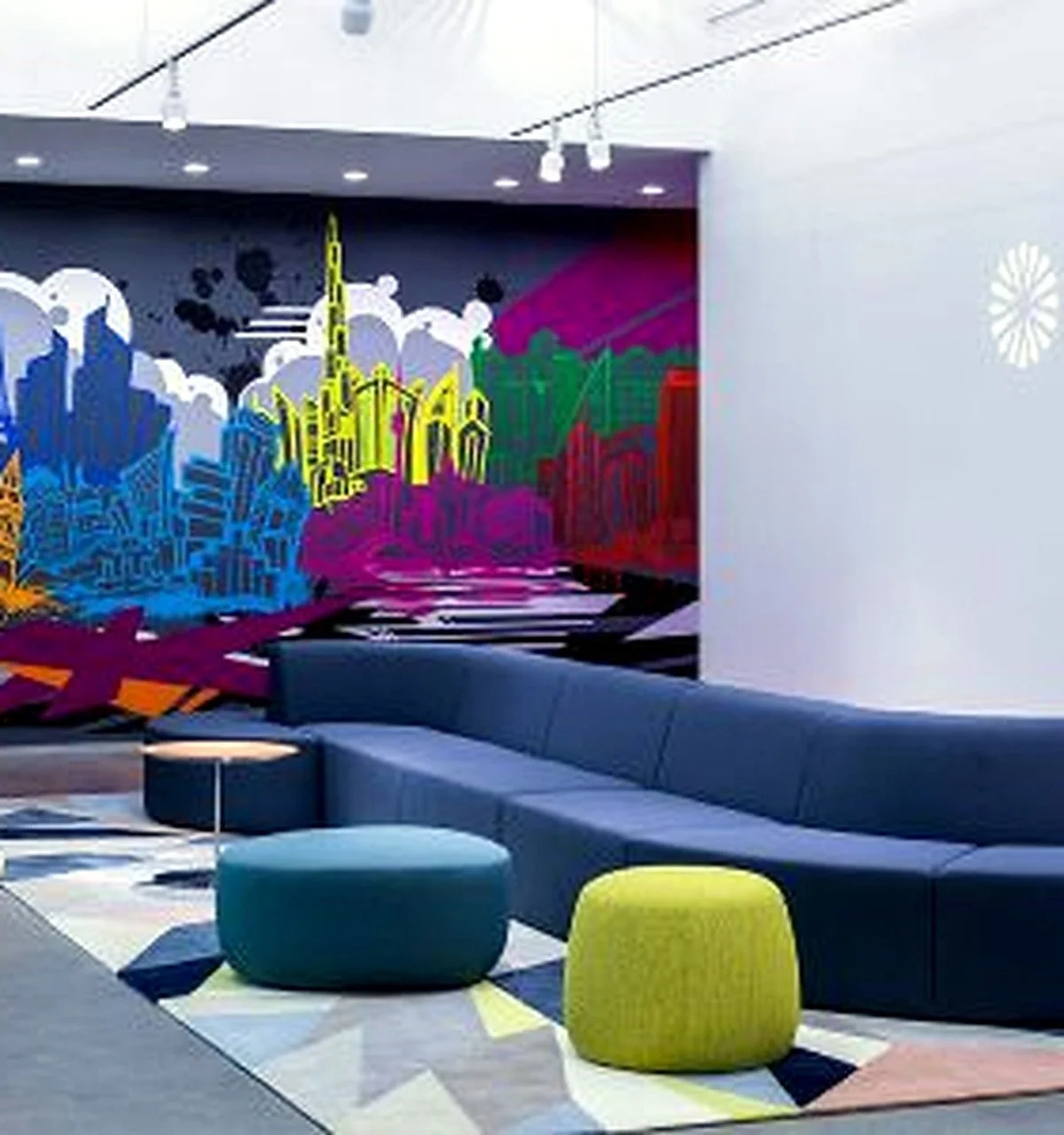 Modern interior with a colorful mural of a cityscape on the wall, curved couch, round ottomans, and contemporary decor.