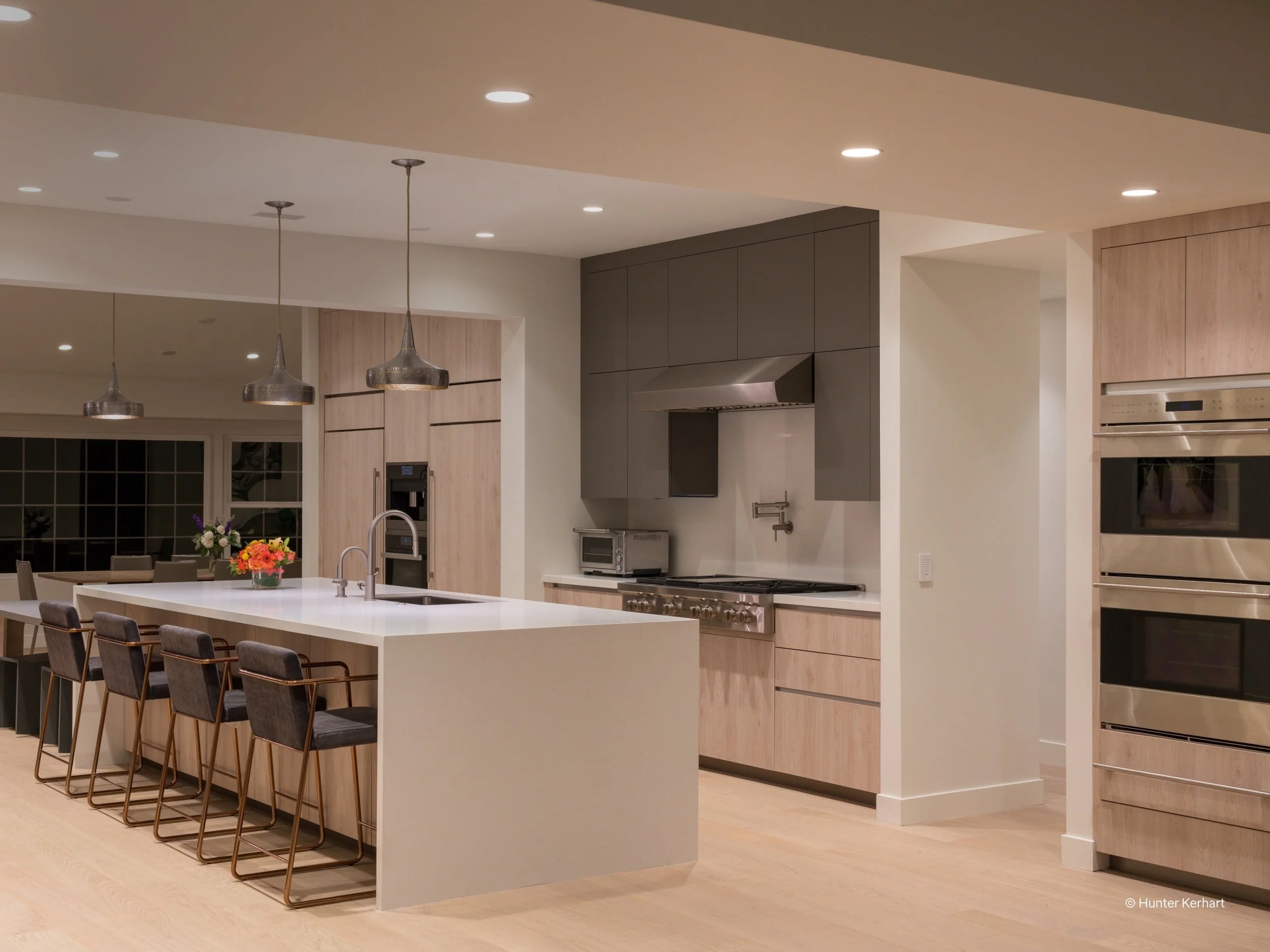 A sleek contemporary kitchen designed with Lutron smart lighting, offering layered illumination for both task and ambiance. Recessed LED downlights provide even overhead lighting, while pendant fixtures above the island deliver focused task lighting
