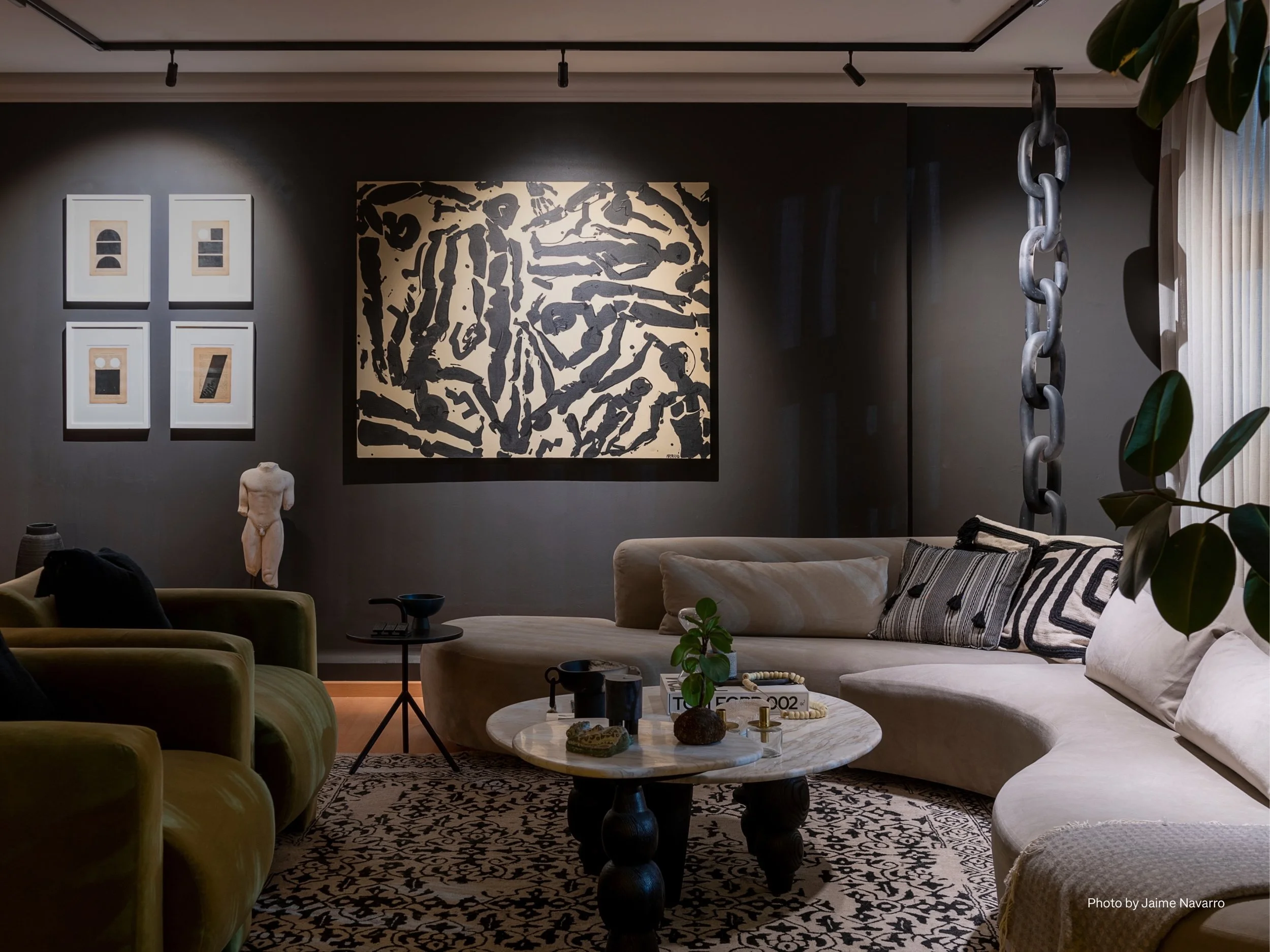A sophisticated living room with Lutron smart lighting control highlighting dramatic modern artwork and creating a gallery-like atmosphere. A curved sectional sofa with textured pillows, sculptural coffee table, and abstract patterned rug bring depth