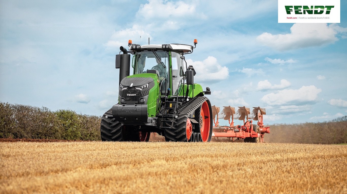 Green Fendt tractor plowing a field under a blue sky.