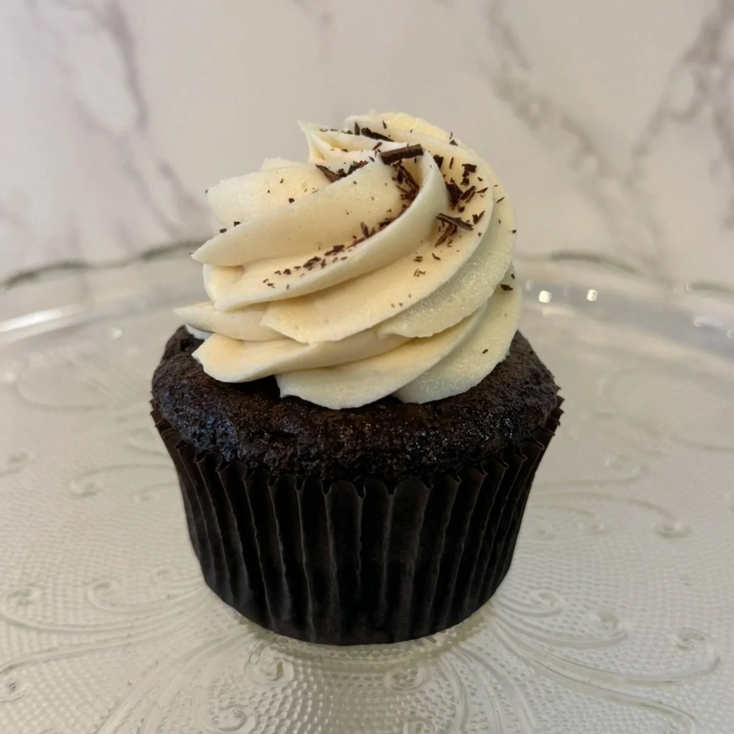 Chocolate cupcake topped with white frosting, a square cookie, and a sprinkle of crumbs.