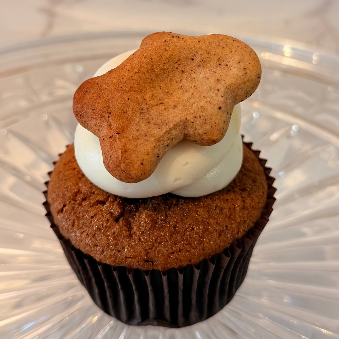 Cupcake with a yellow cake base, black paper wrapper, topped with pink frosting.