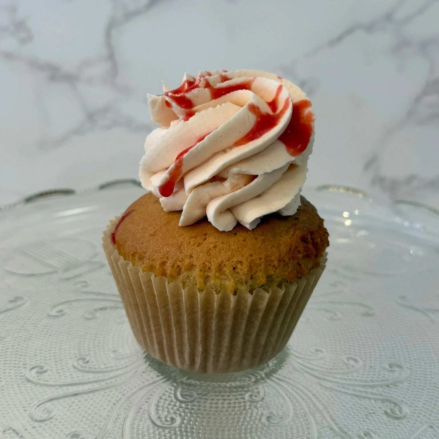 A cupcake topped with white frosting in a ridged paper liner.