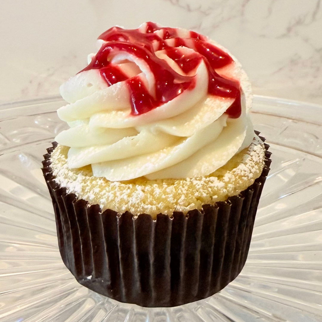 Cupcake with white frosting and a cherry on top, in a black paper liner.