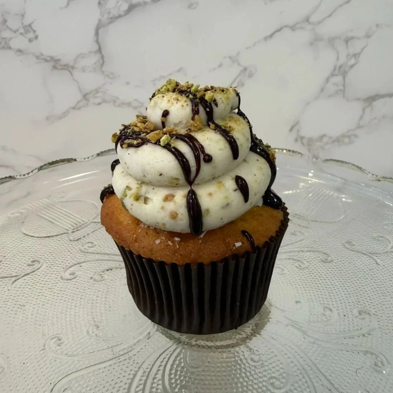 Cupcake with a yellow cake base, black paper wrapper, topped with pink frosting.