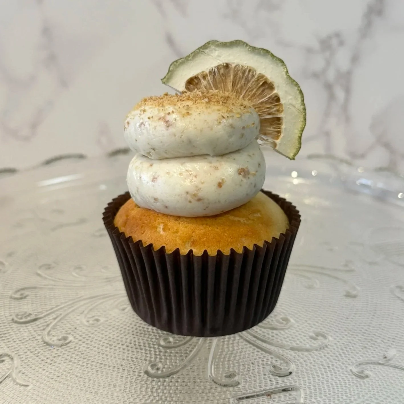 Cupcake with yellow cake, topped with white frosting and lime slice