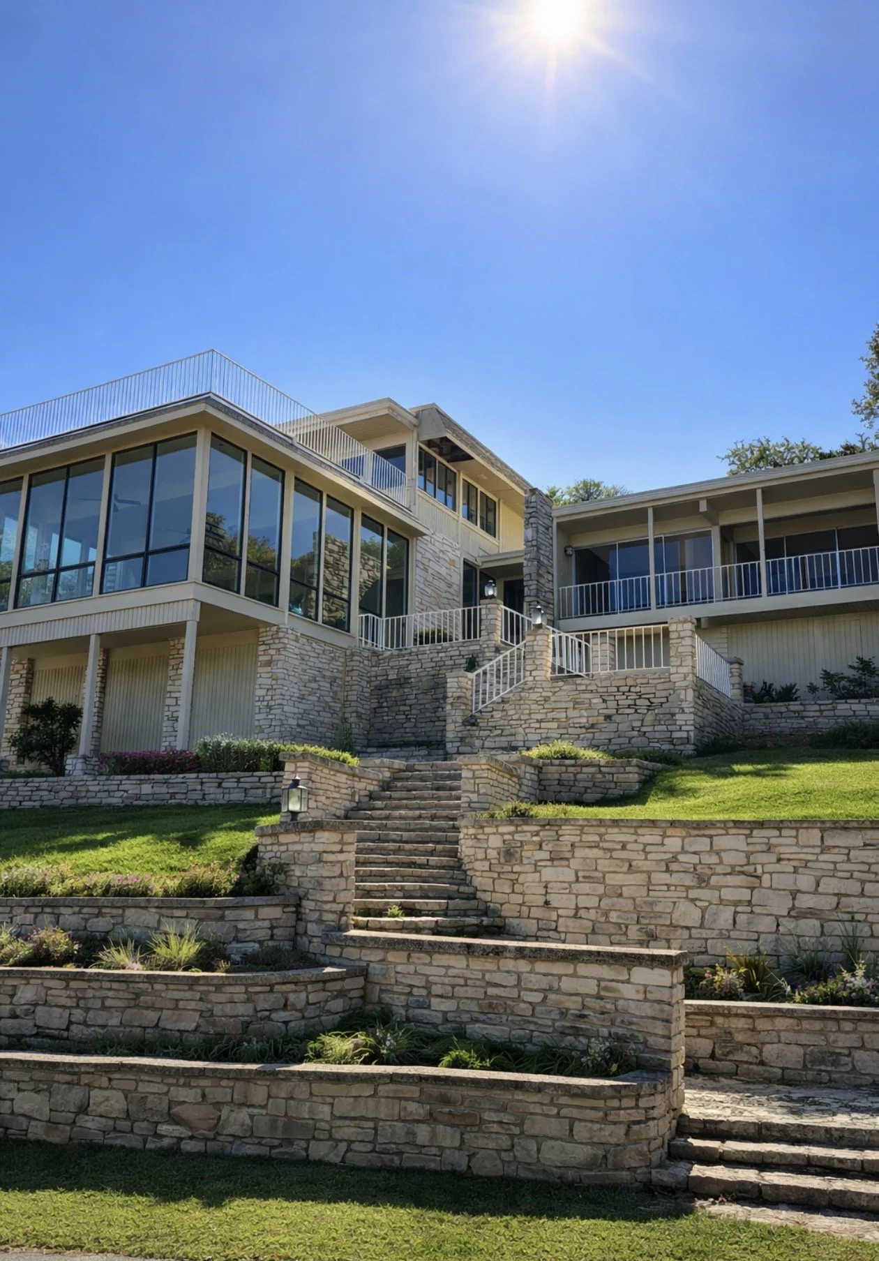 A multi-story house with large windows, stone accents, and a landscaped yard with staircase and green grass.