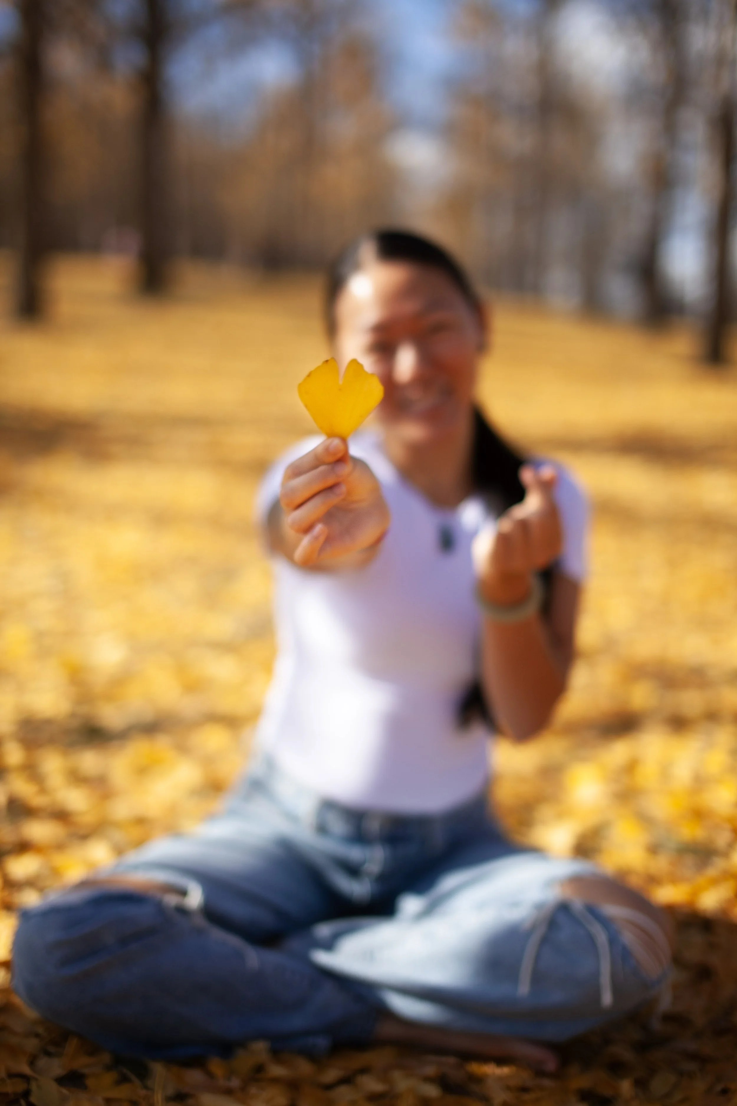 Asian woman holding heart shaped gingko leaf and making heart sign with her fingers.