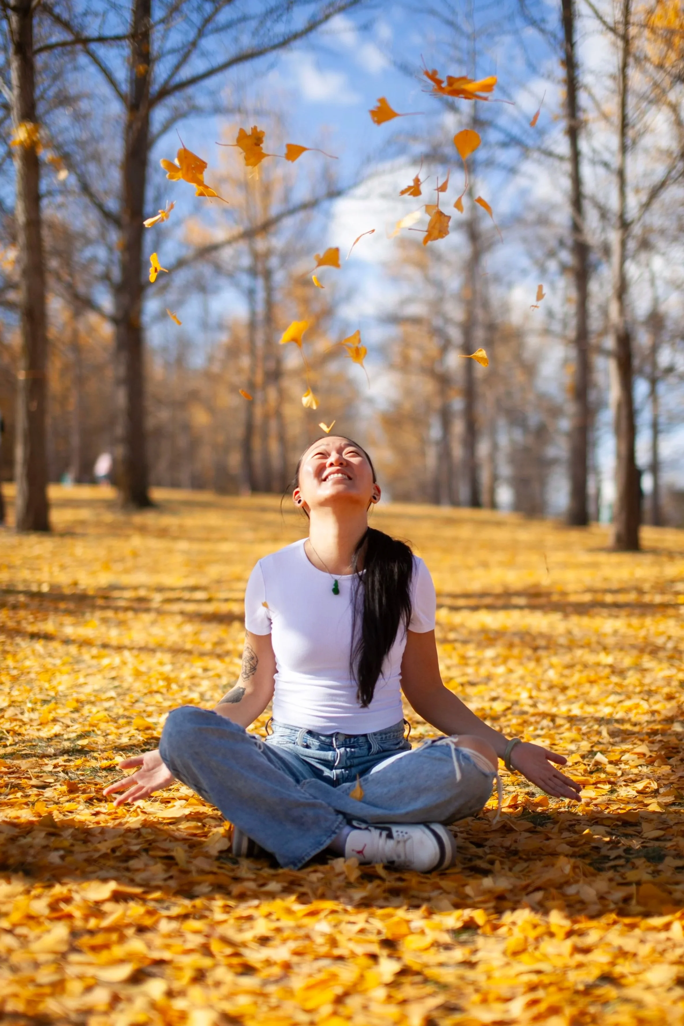 Asian woman in field of gingko trees with golden leaves falling around her.