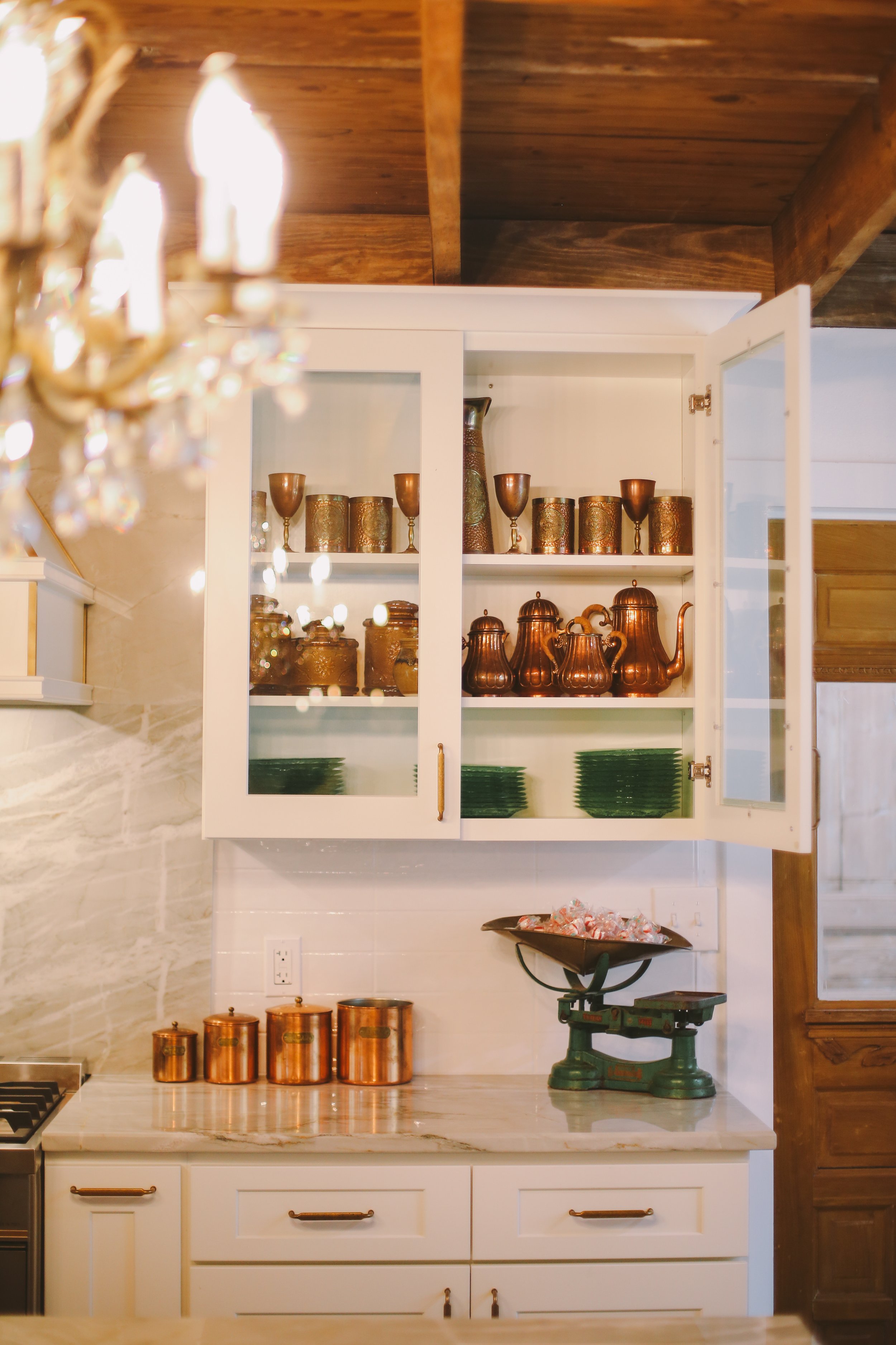 A white wood and glass cabinet showcasing vintage copper drinkware and green glass plates.