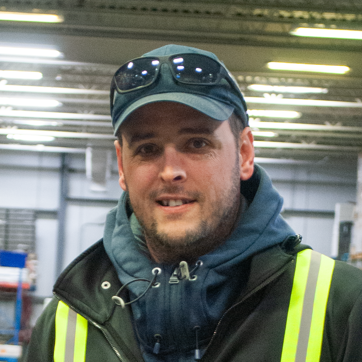Un homme souriant portant une veste à haute visibilité dans un entrepôt intérieur.
