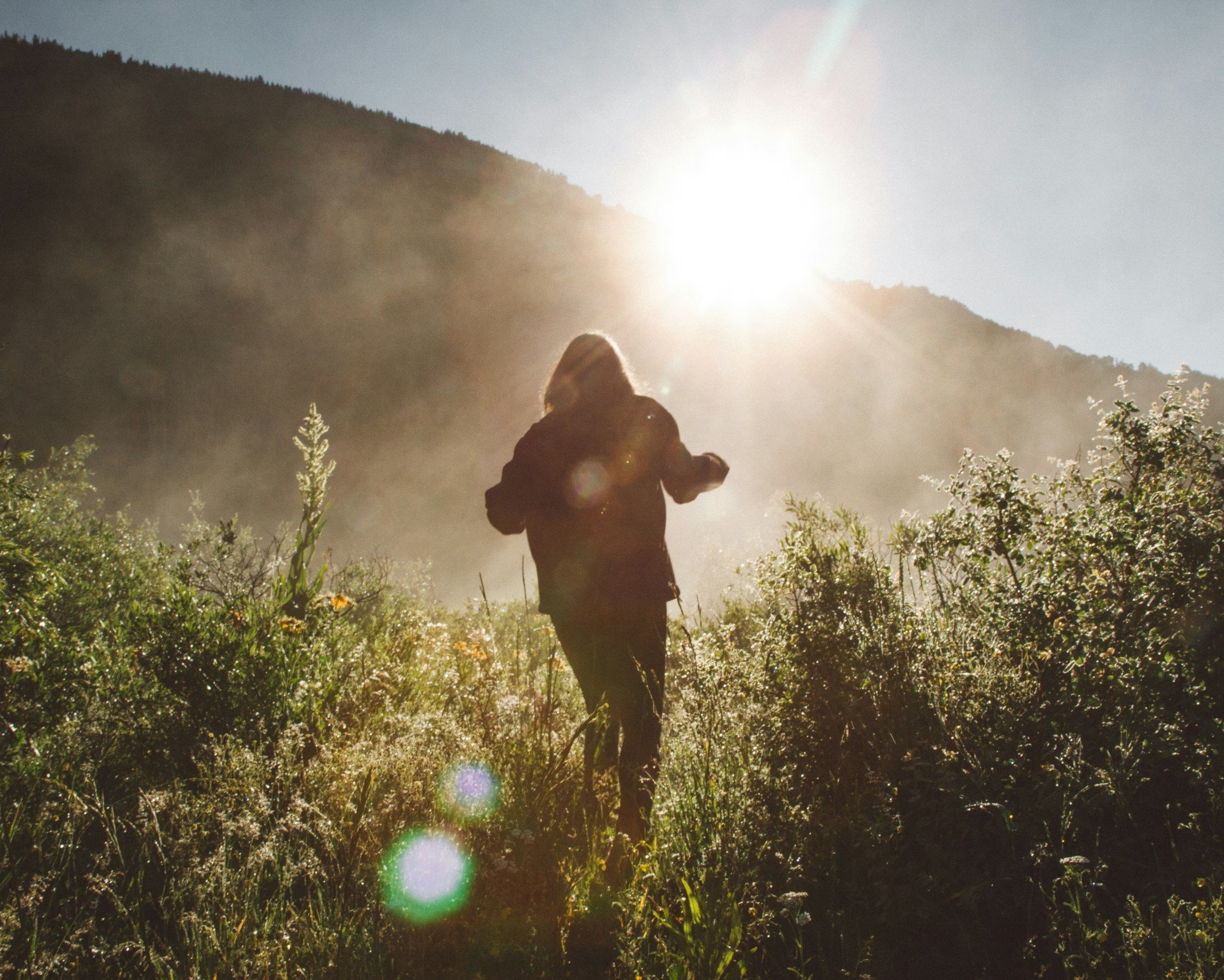 Woman walking through long wildflowers and natural plants on hillside