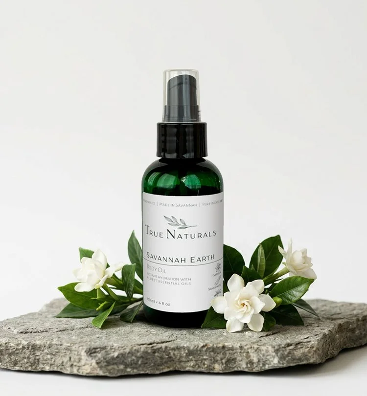 True Naturals Savannah Earth Body Oil on a stone slab with gardenia flowers.  All natural skincare with the power of pure essential oils.