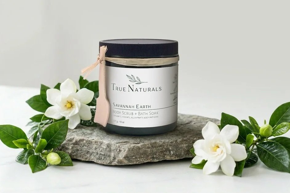 True Naturals SAVANNAH EARTH Body Scrub with gardenias on a stone slab. All natural plant-based skincare.