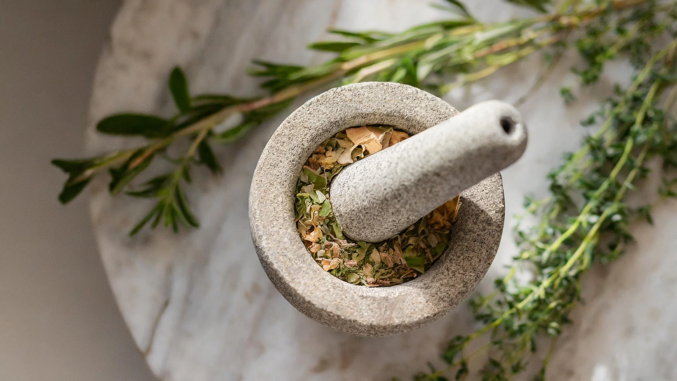 stone mortar and pestle with fresh herbs. True Naturals hand-blended plant-based skincare