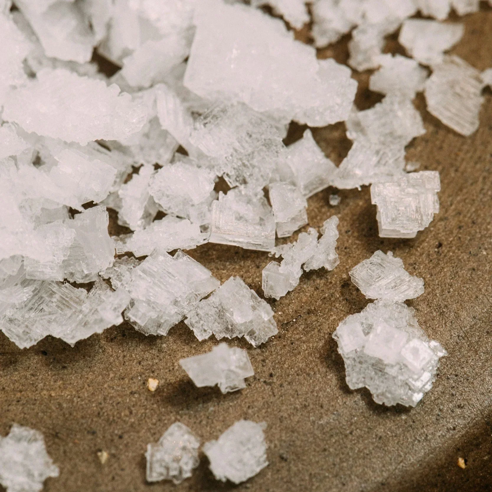 White salt crystals on wood background. True Naturals pure plant-based ingredients.