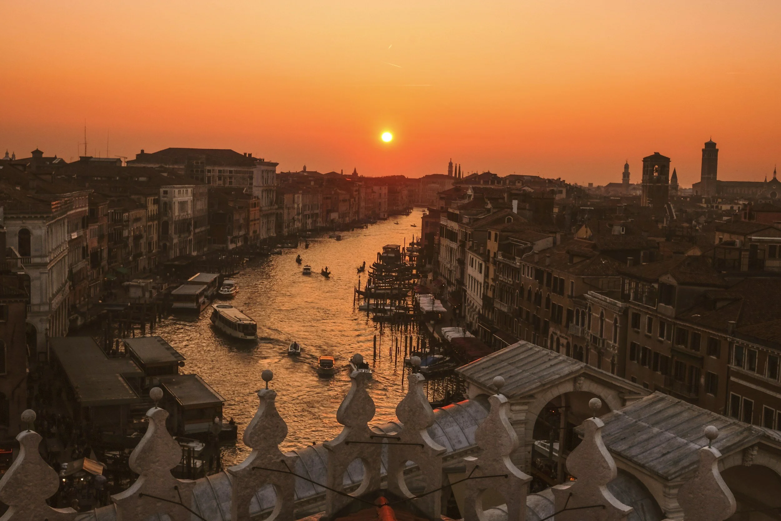 Sunset over Venice with a canal, boats, and historic buildings.