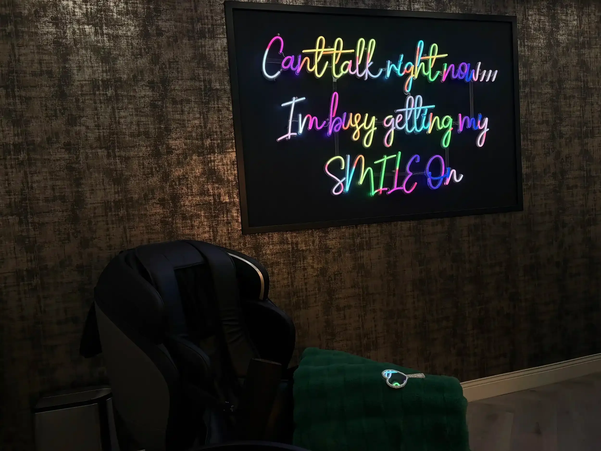 A neon sign reading "Can't talk right now... I'm busy getting my SMILE On" above a massage chair at Smile Bar in Calgary.