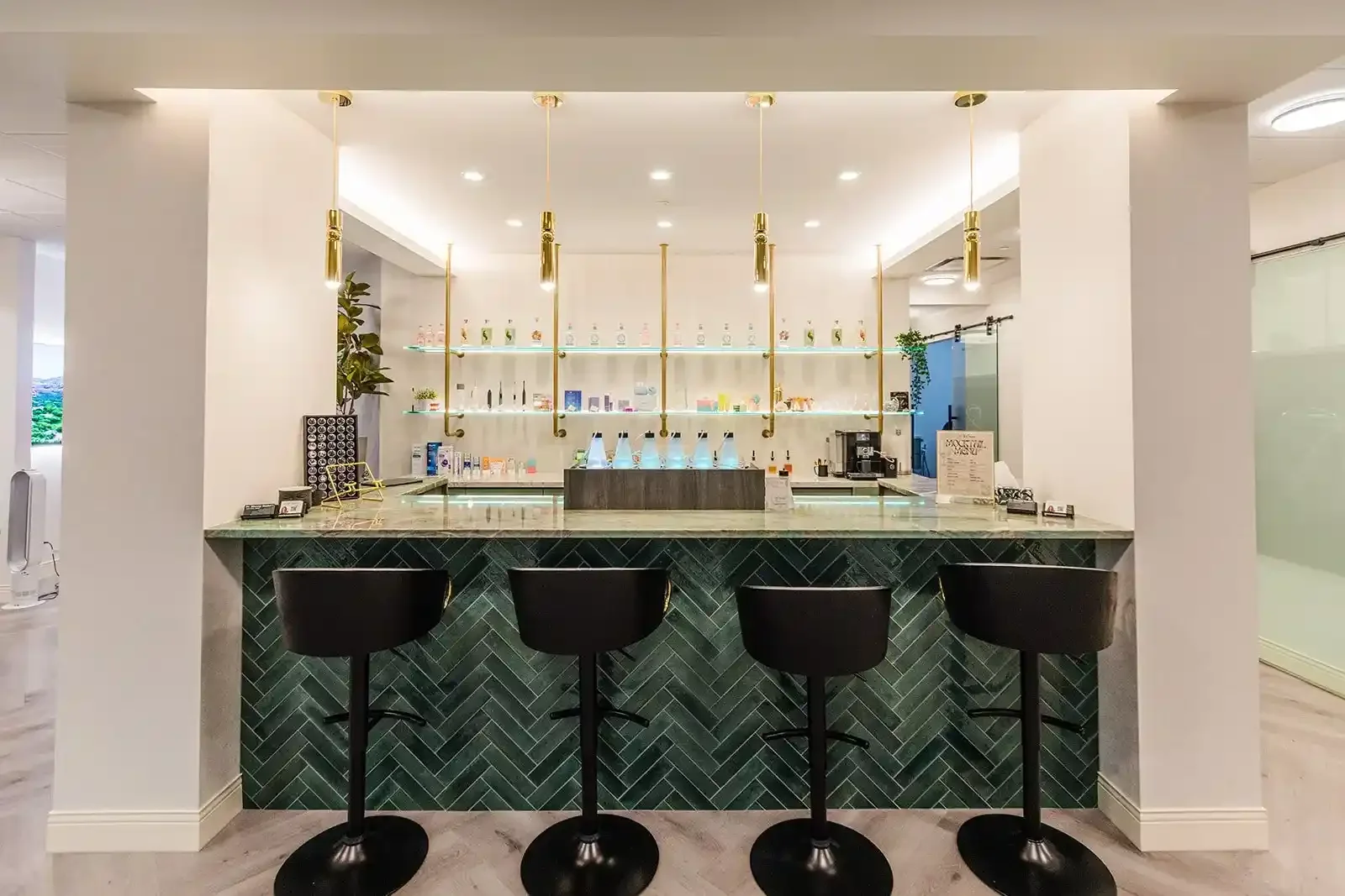 The modern beverage and concierge bar featuring a green tiled counter and black stools at Smile Bar in Calgary.